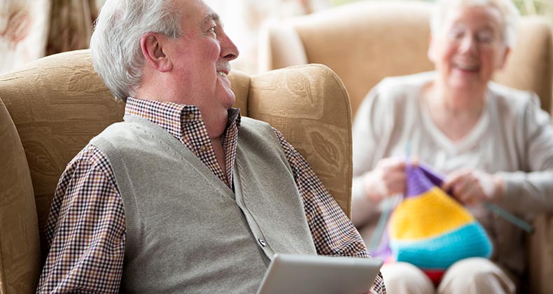 Senior couple at home, husband holding tablet pc wife knitting | iStock.com/SolStock